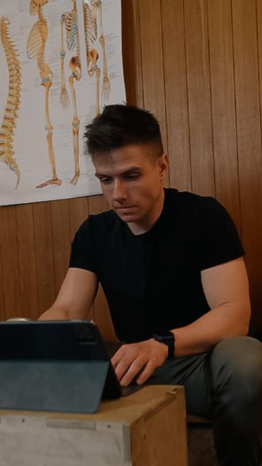 Fizjoterapeuta pracujący na tablecie w gabinecie, w tle plakat anatomiczny kręgosłupa